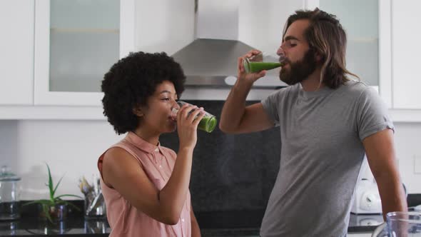 Mixed race couple drinking vegetable smoothie together in the kitchen at home