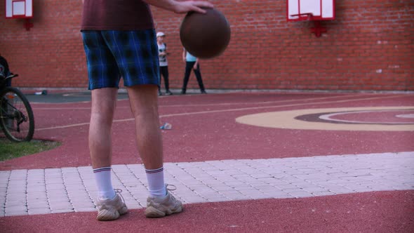 Young Man Standing on the Basketball Playground and Hitting the Ball