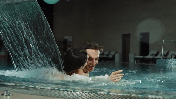 Funny Couple Piggybacking in Spa Pool. Handsome Man and Woman Cuddling Jacuzzi