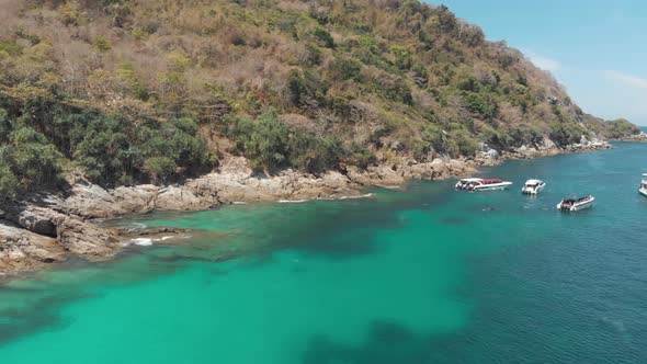 Emerald green waters protecting a coral reef and bordering a rocky shore and boat anchorage