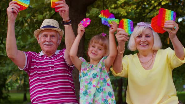 Smiling Senior Grandmother Grandfather with Granddaughter Playing Squeezing Antistress Toy Game