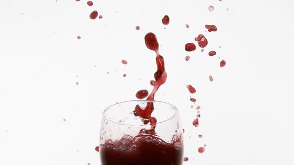 Glass Falling and Red Wine splashing against White Background, Slow Motion