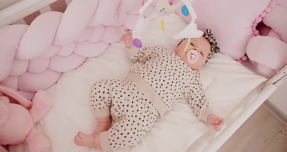 Tiny Newborn Girl Playing With Toys Lying In A Cradle