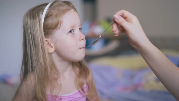Mother Gives Medicine To Cute Girl with Spoon on Bed