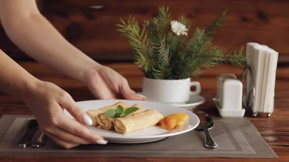 Hands of Waiter Puts White Plate with Delicious Vegan Banana Peach Pancakes Breakfast in Restaurant