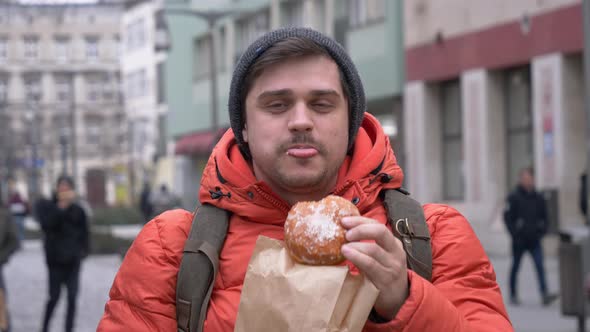 man eating traditional polish donut on city street