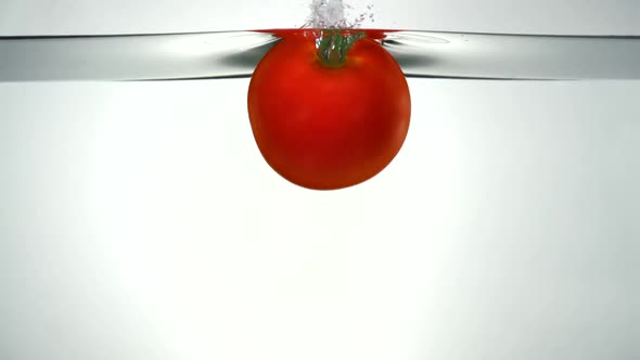 Slo-motion beefsteak tomato falling into water