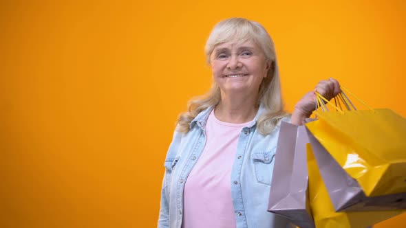 Cheerful Elderly Woman Holding Shopping Bags and Dollar Cash, Consumerism