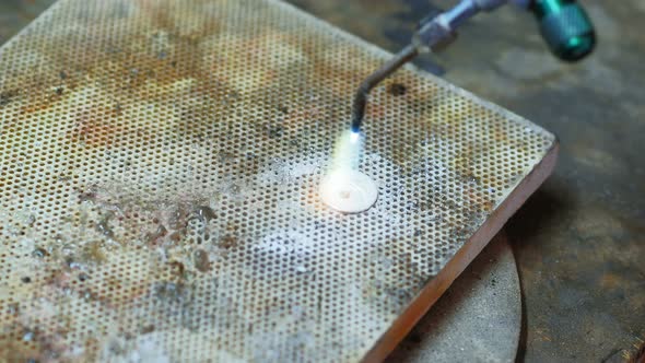 Close-up of Craftswoman blowing a torch to melt metal