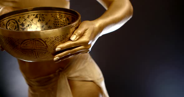 Lady with Golden Skin Performs Belly Dance Holding Bowl