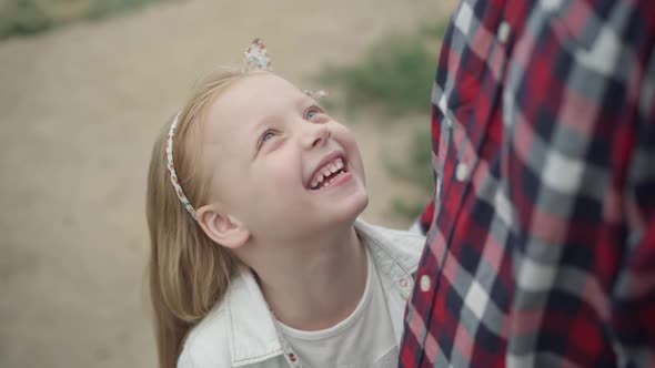 Closeup of Cheerful Laughing Cute Little Girl Looking Up at Unrecognizable Man Caressing Long Blond