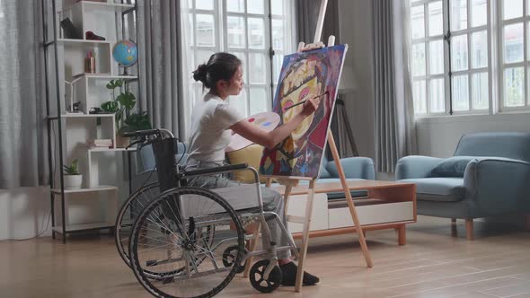 Asian Artist Girl In Wheelchair Holding Paintbrush Mixed Colour And Painting A Girl On The Canvas