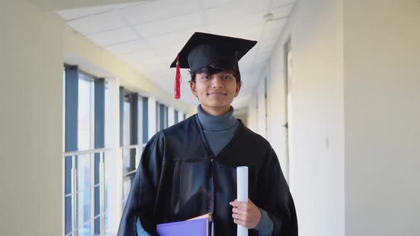 Indian Male Graduate in Mantle Stands with a Diploma and Books in Her Hands and Smiles