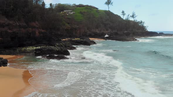 Aerial drone camera shoots ocean waves, beach and house on the mountain at Kauai, Hawaii, USA