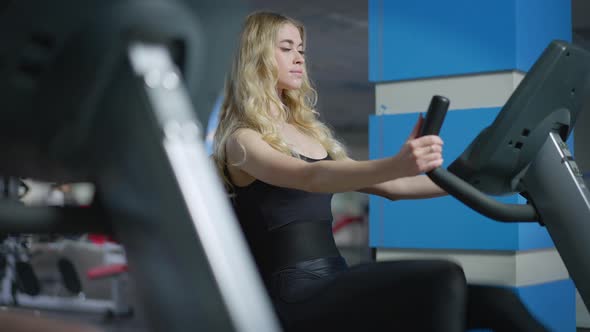 Blond Concentrated Caucasian Sportswoman Riding Exercise Bike in Gym Indoors