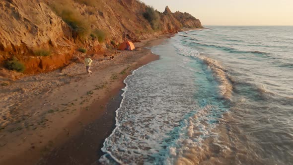 Woman Runs By Long Sandy Beach with Clay Hills Along Sea Cute Dog Follows Girl