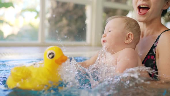 Happy Mother in Red Swimming Suit with Baby Son Surfing Water with Fun in Swimming Pool