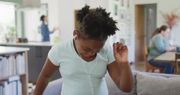 Happy african american girl wearing earphones and dancing in living room