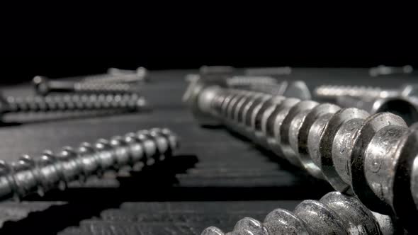 Camera Pans Over Screws Metal Threaded Bolts Fasteners Lying on Table on Black Background