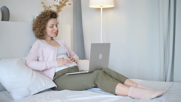 Pregnant Woman Using Laptop Lying On Bed At Home