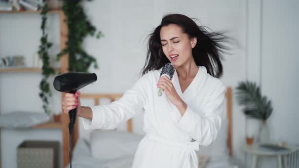 Young Woman in White Bathrobe Dances, Sings and Dries Hair with Hairdryer