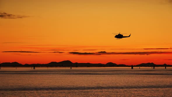 Dark Silhouette of Helicopter Flies at Sunset Above River