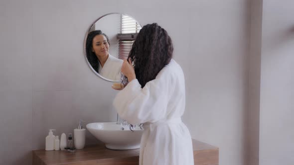 Young Happy Hispanic Woman Stands in Bathroom in Bathrobe Looks to Mirror Combs Thick Long Healthy