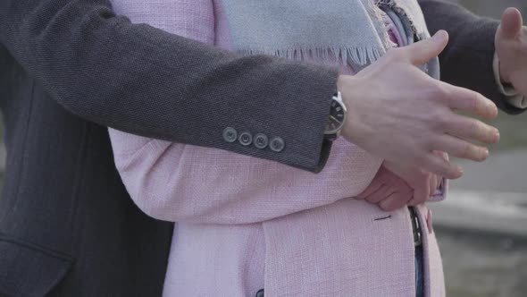 Close-up of Young Male Caucasian Hands Hugging Unrecognizable Woman in Pink Coat. Adult Loving