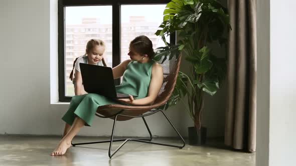 Young Mother and Little Daughter Having Good Time Together and Using Laptop at Home Room Iroi