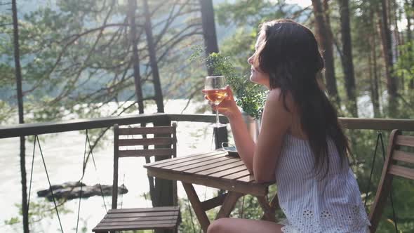 Attractive Brunette with a Glass in Her Hands Enjoying Nature in the Mountains, Sitting on the