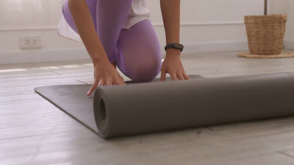 Asian woman's hands rolling up her yoga mat after a workout at the studio.