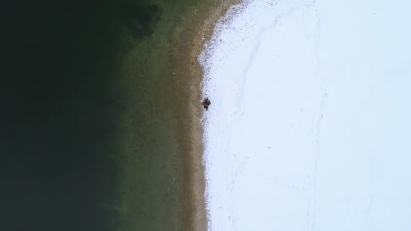 Top down aerial, man walks along Bohinj lakeside in winter, Slovenia.