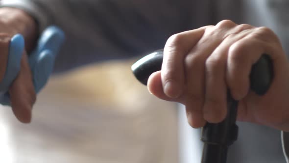 Close-up of a nurse's hand in a glove holds carefully the hands of an old man leaning on a cane. Rec