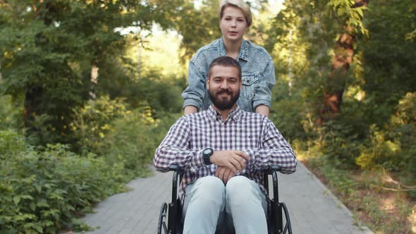 Loving Happy Married Caucasian Couple Disabled Person Man in Wheelchair and a Woman is Taking Him