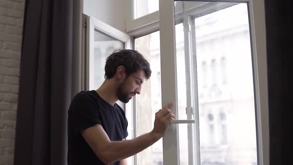 Man is Cleaning Window Cleans Surface and Uses a Rag Standing in Modern Apartment