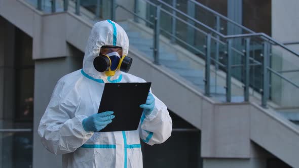 A Portrait of a Young Man in a Protective Suit, Respirator, Gloves and Safety Glasses Holds a Folder