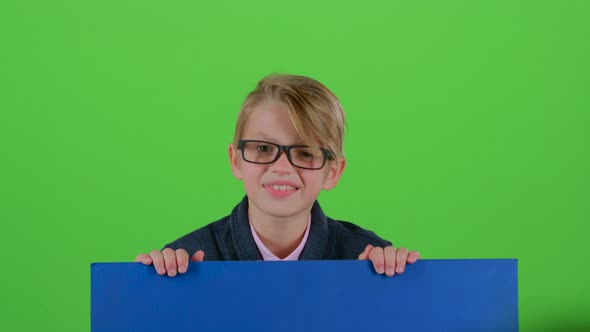 Child Boy in the Glasses Looks Out From Under the Board Holding on To Her on a Green Screen