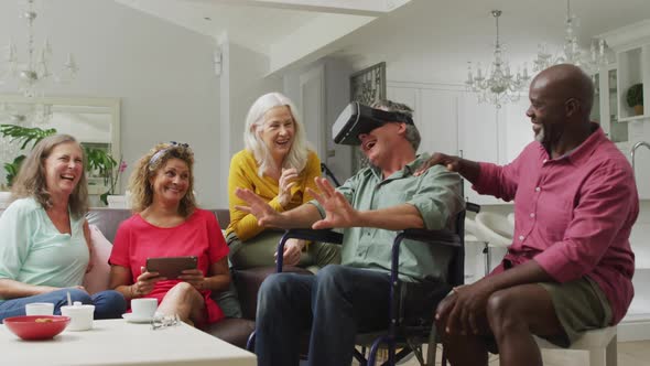 Video of happy senior man in wheelchair using vr headset and having fun with diverse friends