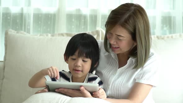 Asian Mother And Her Son Using Tablet On Sofa