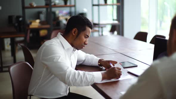 African American Business Man Studying Paper Document and Signing Contract Sitting at Office Desk