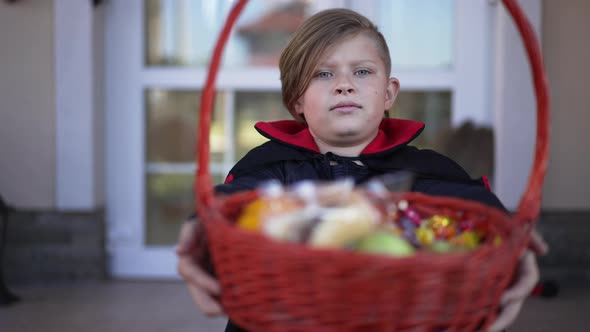 Front View Portrait of Cute Boy Posing with Trick or Treat Basket Looking at Camera Sitting Outdoors
