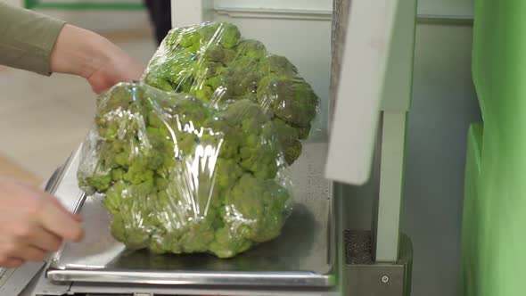 Closeup of a Woman Weighing Broccoli on Scales in a Supermarket