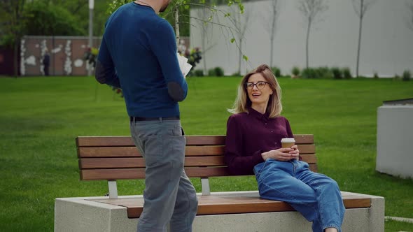 Handsome man brings lunch for colleague sitting on a bench in the park. Work Coffee Break.