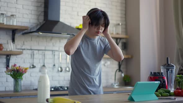 Middle Shot of Young Asian Man Putting on Headphones and Talking at Tablet Video Chat