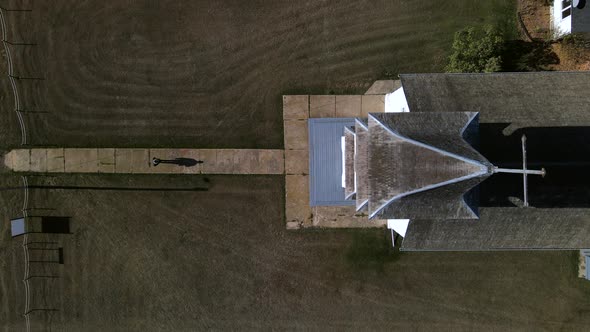 Lonely person walking along narrow path towards old wooden country church in American prairie. Top-d