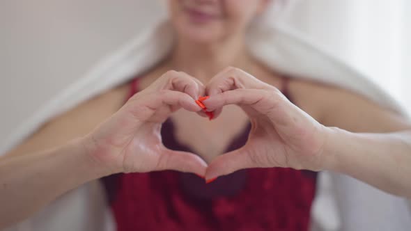 Closeup Heart Shape Gesture with Unrecognizable Blurred Smiling Mature Woman at Background