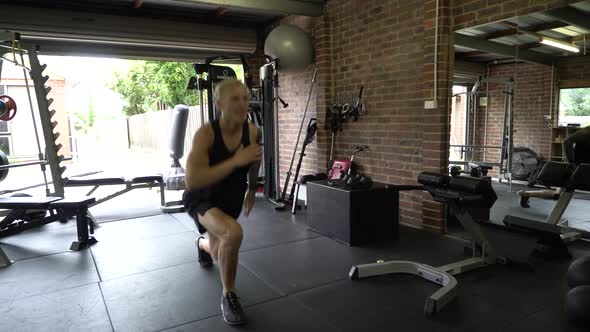 Tattooed man in home gym split jump lunges from front