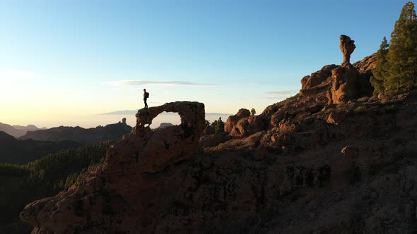 Man On Rock Arch Looking At Mountains