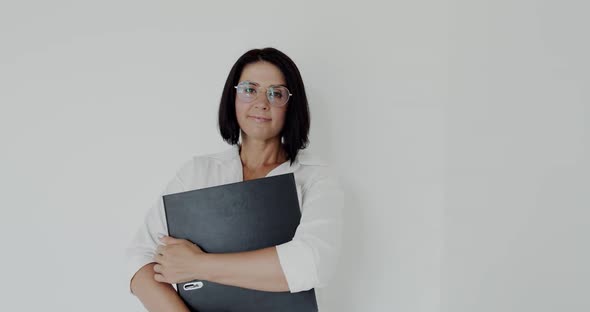 Teacher with Glasses and Big Folder in Hands Smiling at Camera on Background
