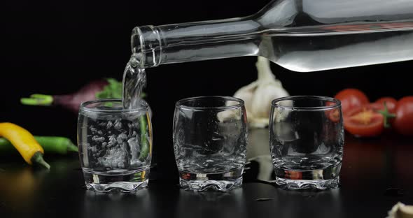 Pour Alcohol Vodka From a Bottle in Three Shot Glass. Background with Vegetables